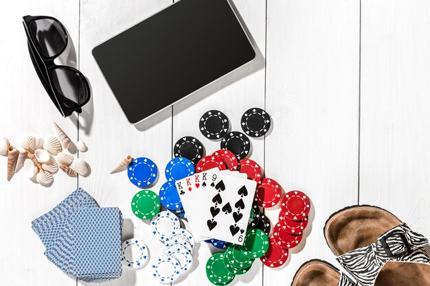 Gambling. Poker chips, cards and the dice nearby tablet on white wooden table. Top view. Copyspace. Poker. Summer
