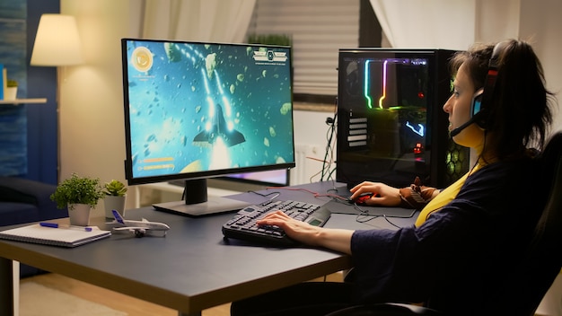 Геймер играет в онлайн-видеоигры в космические стрелялки, используя мощный компьютер и клавиатуру RGB
