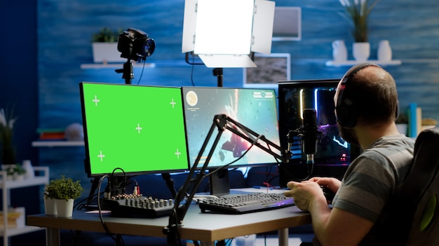 Gamer streaming online videogames on professional powerful computer with green screen, mock up, chroma key display. Streamer playing space shooter game at isolated desktop holding wireles controller