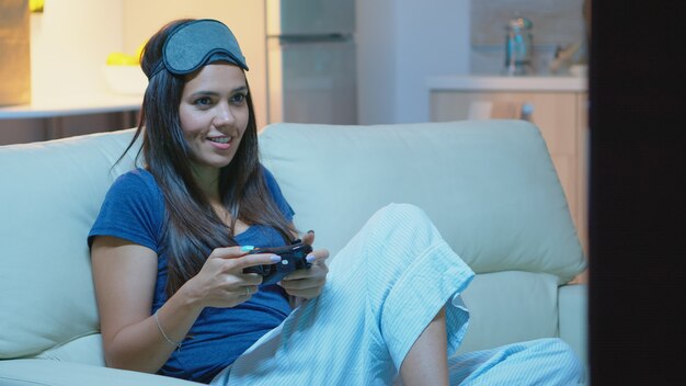 リビングルームのソファに座ってコンソールでビデオゲームをプレイするジョイスティックを使用するゲーマー。コントローラーゲームパッドキーパッドプレイステーションゲームを使用し、電子ゲームに勝つことを楽しんでいる興奮した決心した女性