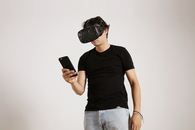 Un giocatore in occhiali vr e t-shirt nera normale guardando il suo smartphone isolato su bianco
