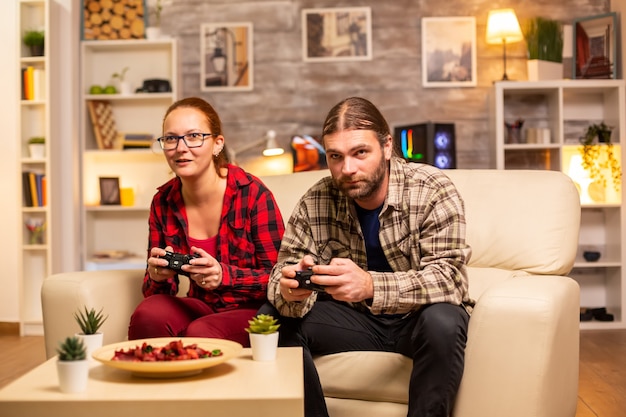 Gamers couple playing video games on the TV with wireless controllers in hands.