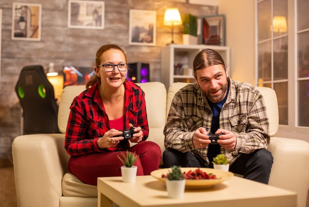 Gamers couple playing video games on the TV with wireless controllers in hands.