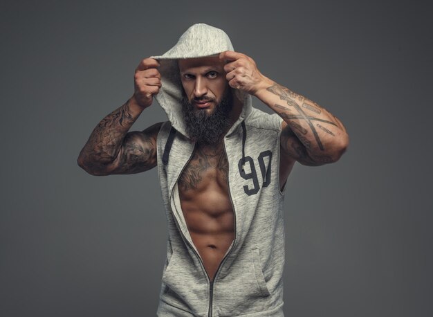 Gangsta tattooed muscular man in a hood. Isolated on grey background.