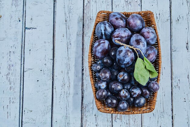 Garden plums in a basket on a blue background. High quality photo