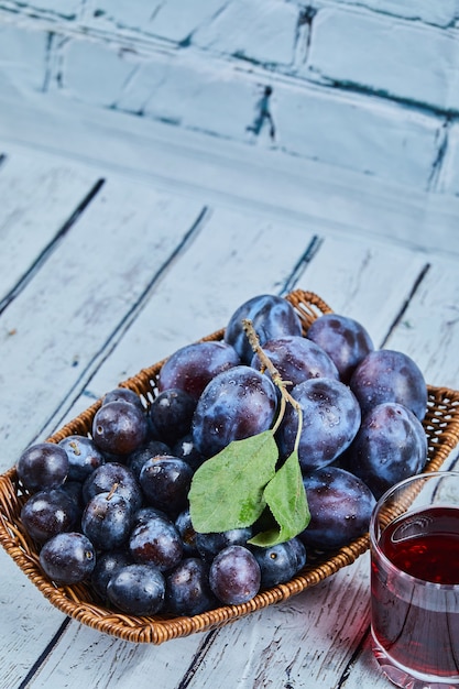 Garden plums in a basket on a blue background with a glass of juice. High quality photo