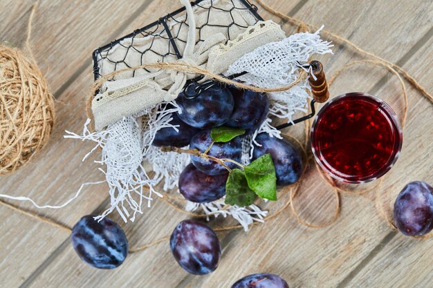 Garden plums in a basket on a wooden table with a glass of juice. High quality photo