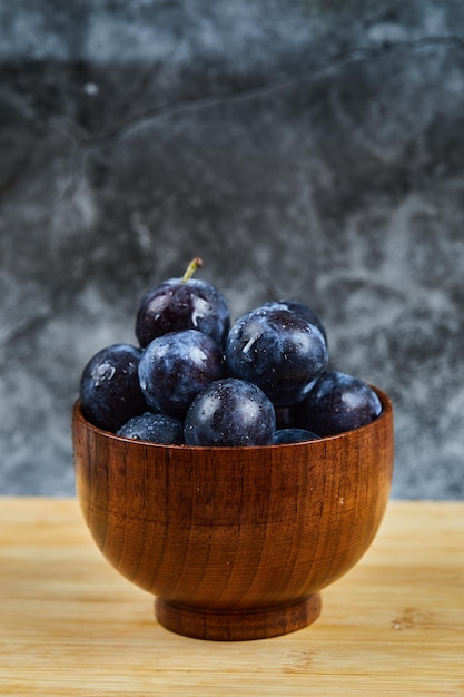 Garden plums on bowl on wooden table.