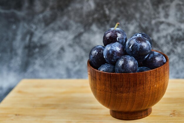 Garden plums on bowl on wooden table.
