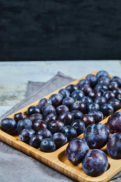 Garden plums on wooden platter and on black.