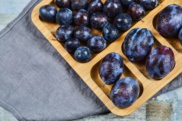 Garden plums on wooden platter with gray tablecloth.