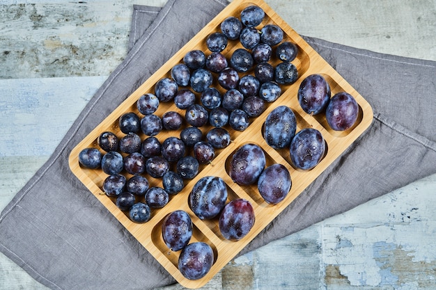 Garden plums on wooden platter with gray tablecloth.