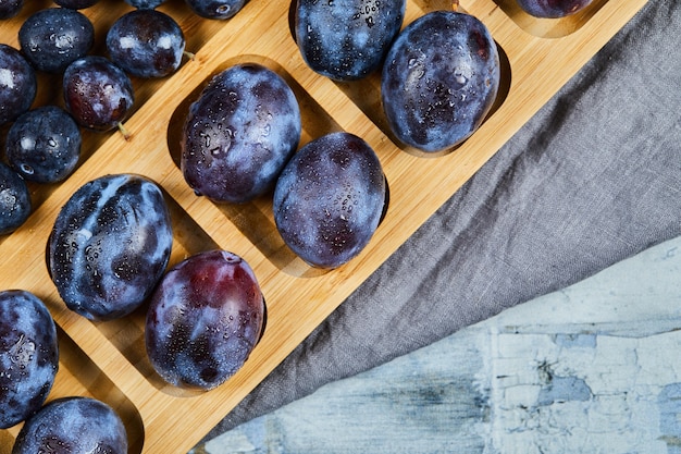 Garden plums on wooden platter with gray tablecloth.