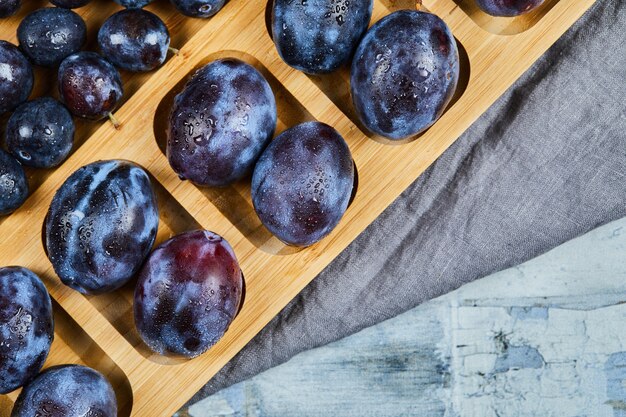 Garden plums on wooden platter with gray tablecloth.