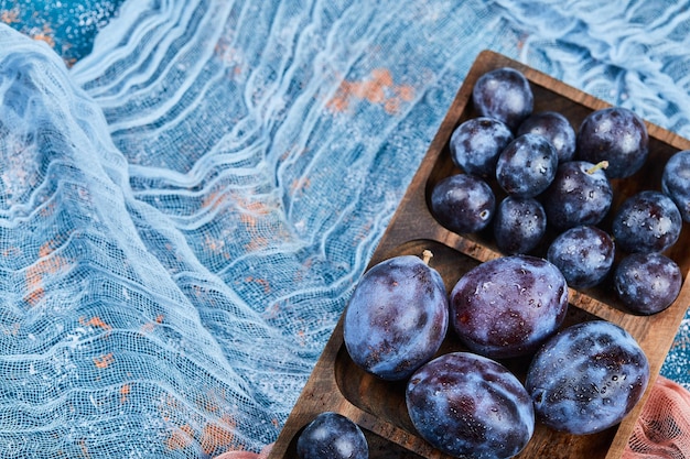 Free photo garden plums on wooden platter with tablecloth.