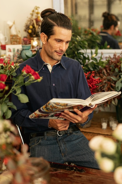 Free photo gardener reading from a book and being surrounded by plants