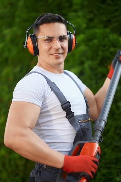 Gardener standing near hedge with electric trimmer in hands