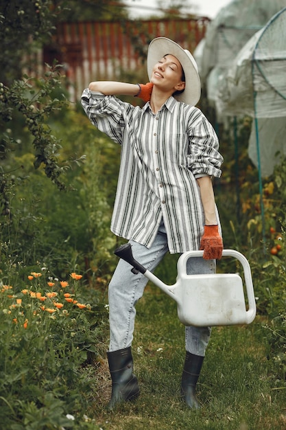 Бесплатное фото Садоводство летом. женщина поливает цветы из лейки. девушка в шляпе.