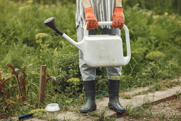 Gardening in summer. Woman watering flowers with a watering can. Girl wearing a hat.