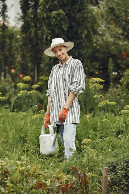 Садоводство летом. Женщина поливает цветы из лейки. Девушка в шляпе.