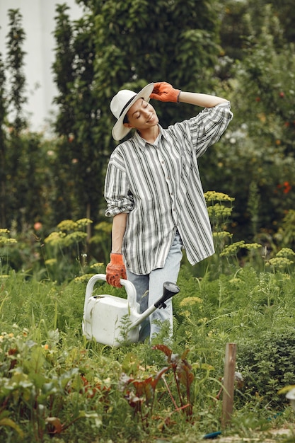 Gardening in summer. Woman watering flowers with a watering can. Girl wearing a hat.