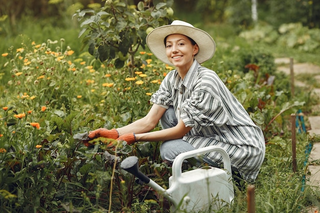 Gardening in summer. Woman watering flowers with a watering can. Girl wearing a hat.