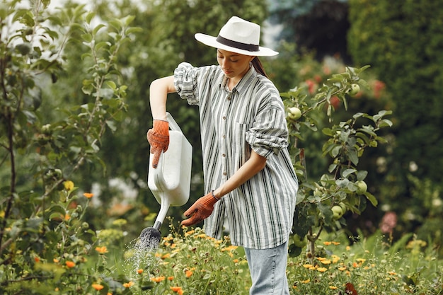 Gardening in summer. Woman watering flowers with a watering can. Girl wearing a hat.