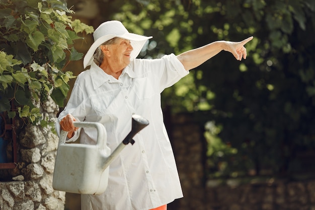 Gardening in summer. Woman watering flowers with a watering can. Old woman wearing a hat.