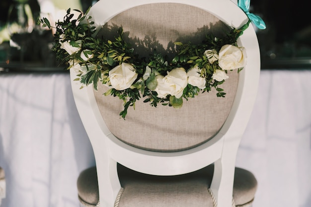 Garland of beautiful white roses hangs on the back of grey chair