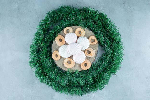 Garland wrapped around a board with cookies and dry apple slices on marble.