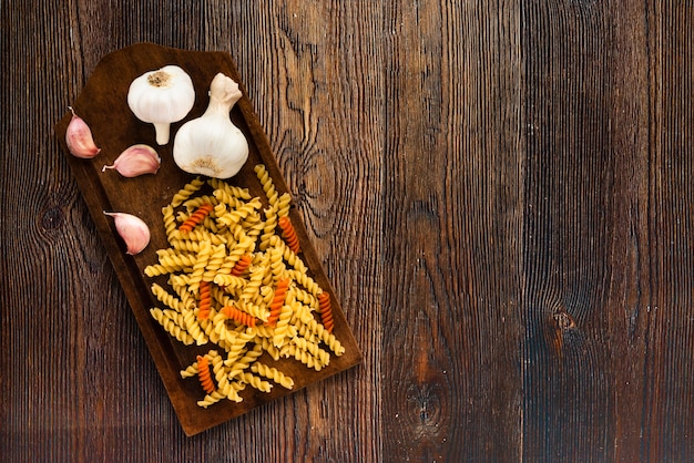 Free photo garlic and fusilli pasta on cutting board over wooden textured background