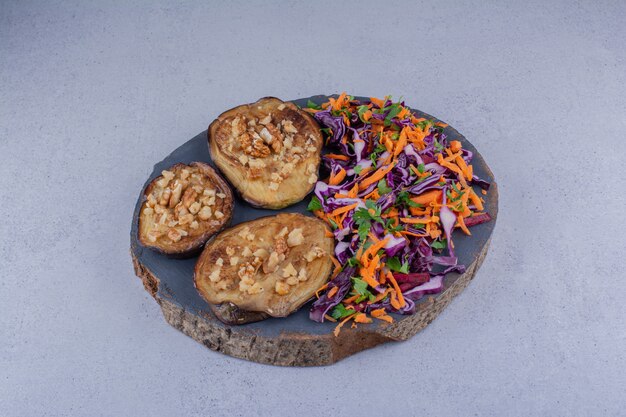 Garlic garnished fried eggplant slices and a portion of salad on marble background.