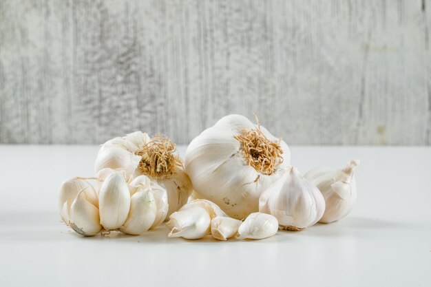 Garlic heads and cloves on a grunge and white surface. side view.