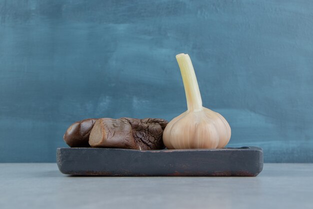 Garlic and pickles eggplant on the wooden plate on the marble surface