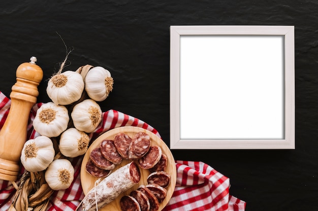 Free photo garlic and sausage near spice and empty frame