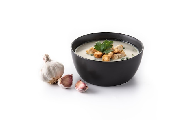 Garlic soup topped with croutons in black bowl isolated on white background