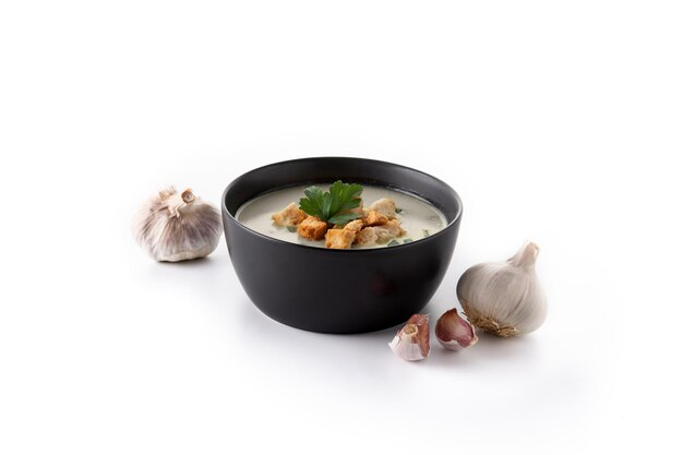 Garlic soup topped with croutons in black bowl isolated on white background