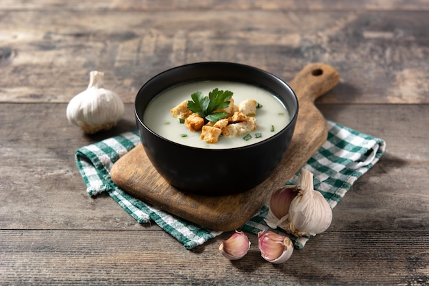 Garlic soup topped with croutons in black bowl on wooden table