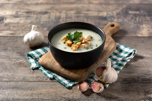 Garlic soup topped with croutons in black bowl on wooden table