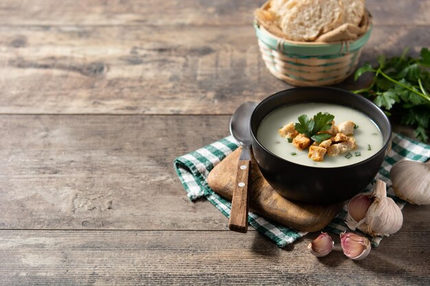 Garlic soup topped with croutons in black bowl on wooden table