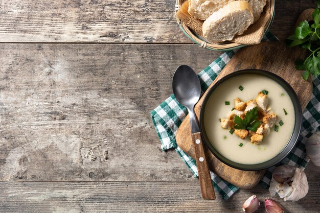 Garlic soup topped with croutons in black bowl on wooden table