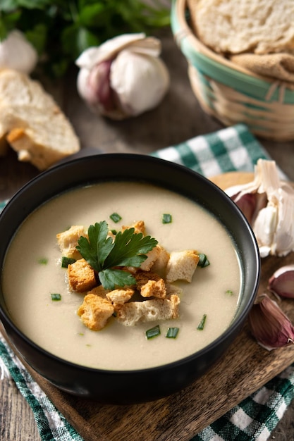 Garlic soup topped with croutons in bowl on wooden table