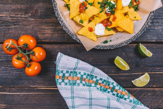Garnished tasty mexican nachos in plate with lemon slices and cherry tomatoes on brown wooden desk