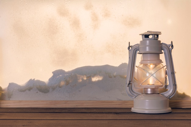 Gas lantern on wooden board near heap of snow through window