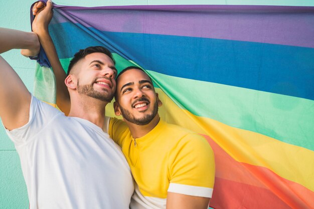 포용과 무지개 깃발로 그들의 사랑을 보여주는 게이 커플.