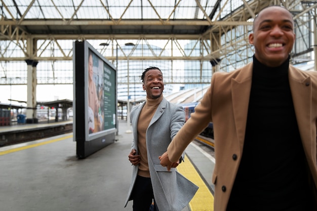 Free photo gay couple holding hands at the train station while on a date