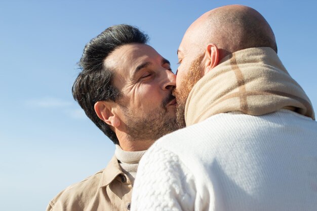 Gay couple kissing against blue sky