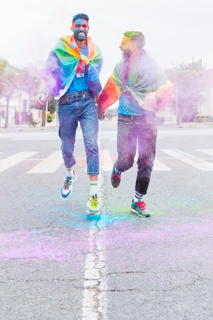 Gay couple in multicolored Holi powder running down road 