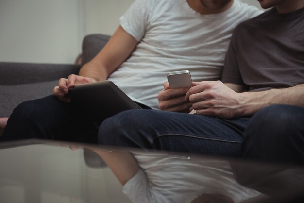Гей-пара сидит на диване и смотрит на цифровой планшет