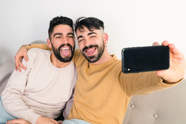 Gay couple sticking out their tongue while taking self portrait on smart phone